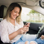 Smiling person using a phone in the driver's seat of a parked car
