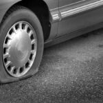 A car with a flat tire is stranded on a road.