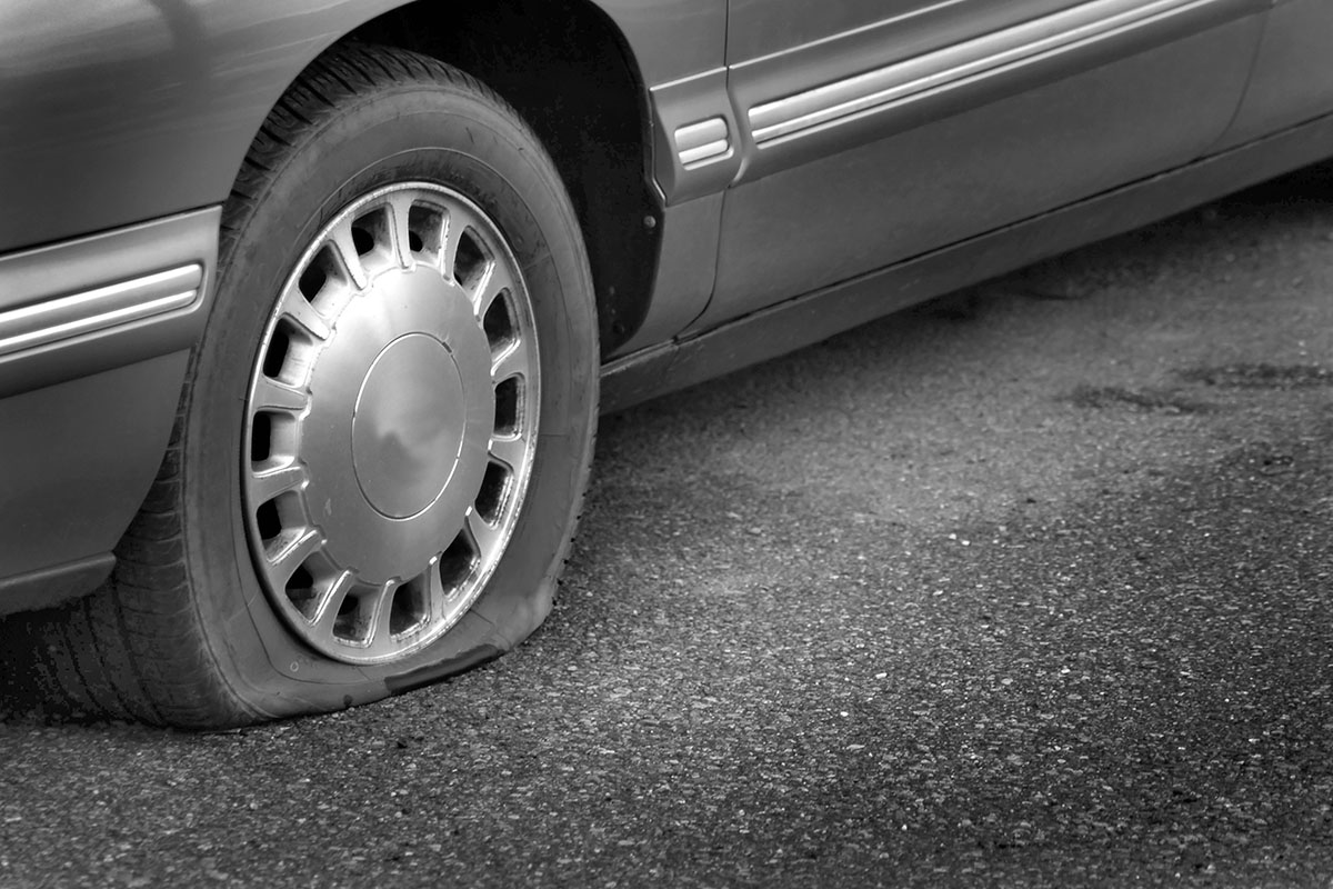 A car with a flat tire is stranded on a road.