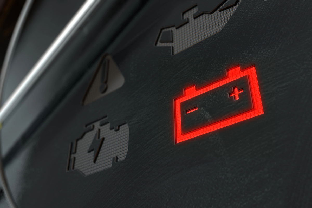 A close-up of a vehicle dashboard displaying a glowing red battery warning icon, indicating a potential issue with the battery. Other warning symbols are faintly visible in the background.
