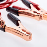 Close-up of copper battery jumper cables with red and black insulated grips, positioned on a white background.
