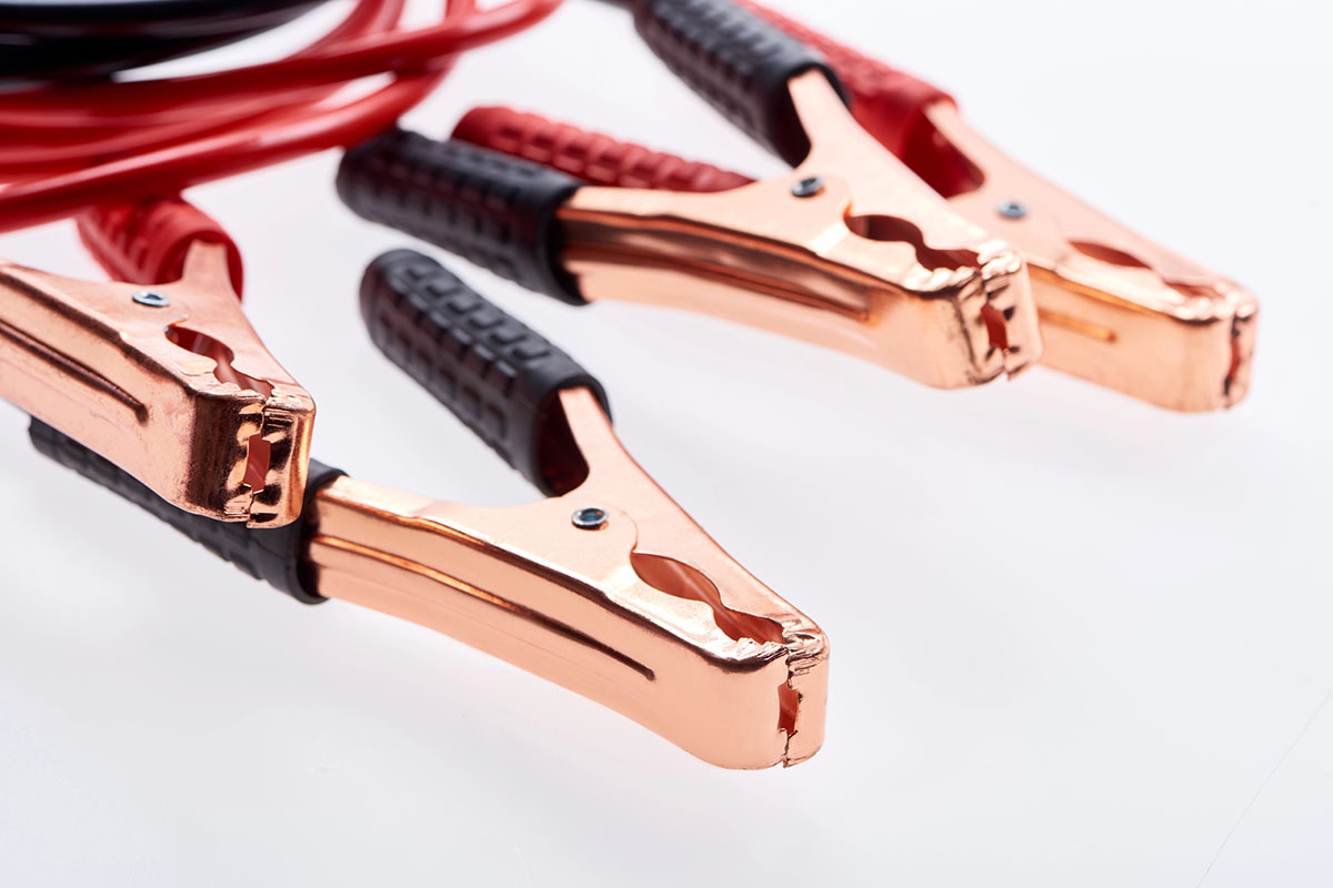 Close-up of copper battery jumper cables with red and black insulated grips, positioned on a white background.