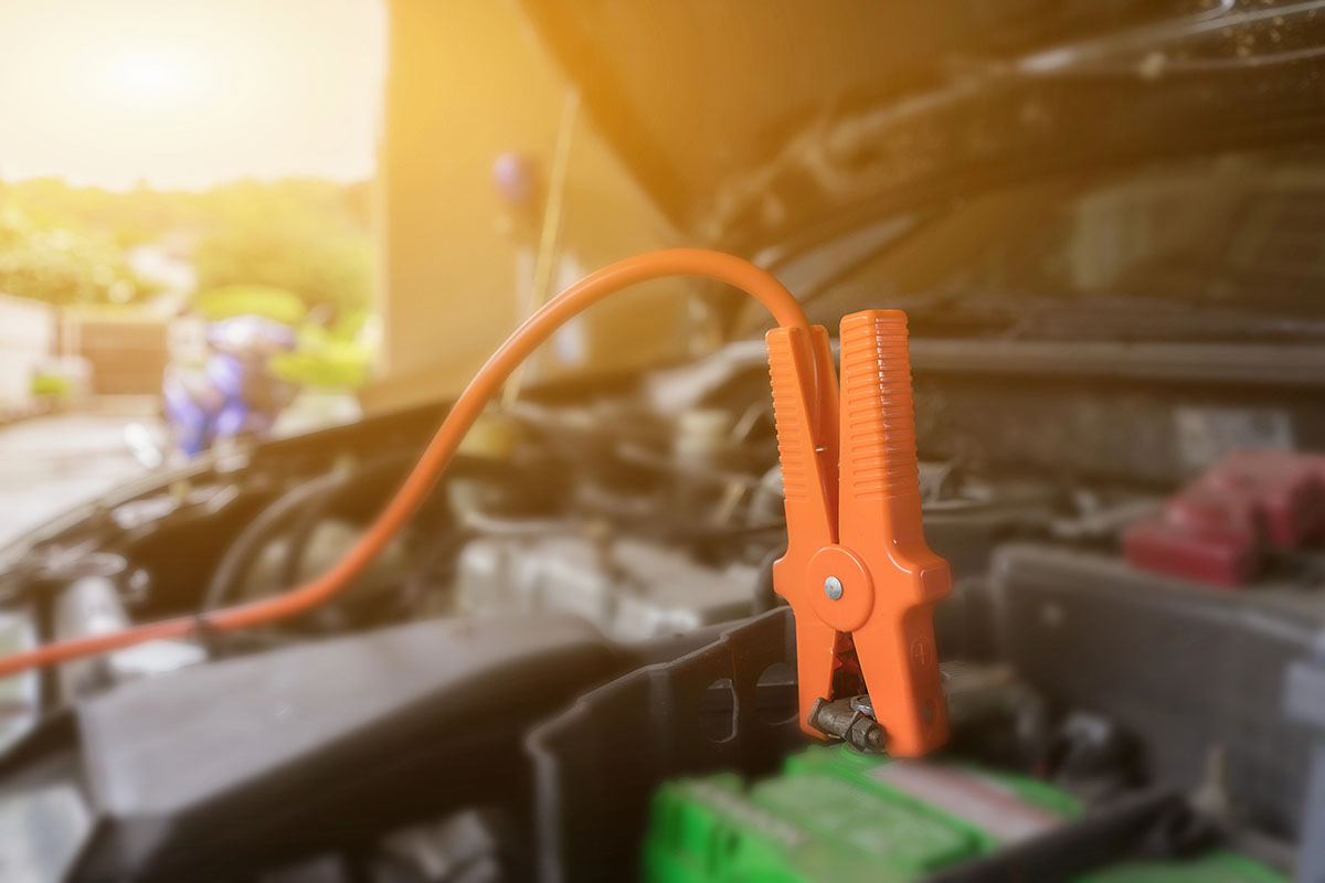 An orange jumper cable clamp attached to a car battery terminal inside an open engine bay.