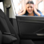 View from inside a vehicle showing a car key fob left on the driver's seat, while a stressed woman holds her head outside the window after locking herself out.